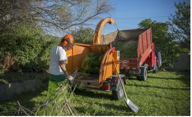 Un opérateur casqué alimente le broyeur, la benne attelée derrière lui